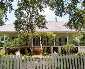 The main house at Oakland Plantation, Cane River Creole National Historical Park, framed by flowering trees and a white picket fence.