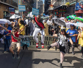 Participants in the French Quarter Festival parade hold signs and dance in the street.