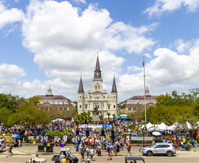 Crowds of people line the streets for the French Quarter Festival in New Orleans, with St. Louis Cathedral in the background.