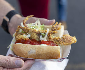 Hands hold a seafood po’boy topped with lettuce and a bright red sauce.
