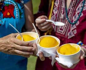 Hands hold three bright orange mango freezes at the New Orleans Jazz &amp; Heritage Festival.