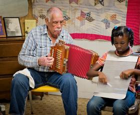 An adult teaches a child to play a washboard instrument.