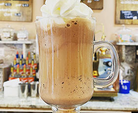 A coffee drink topped with a pile of whipped cream sits in a decorative glass on the counter of Angelo Brocato in New Orleans.