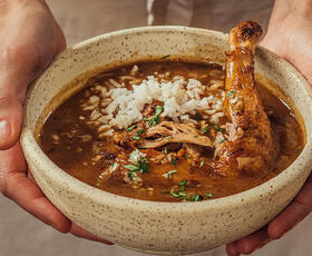A pair of hands present a bowl filled with rice and chicken in a red sauce from the Mosquito Supper Club in New Orleans.