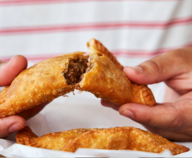 Hands break apart a perfectly fried meat pie.