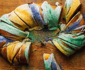 A sliced traditional king cake atop a cutting board.