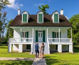 A couple stands in front of the home at E.D. White Historic Site, a white building with green shutters.
