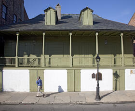Man walking past a sage-green building with a large porch