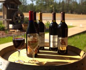 Bottles of red wine sit on a barrel behind a full glass of red wine and a full glass of white wine.