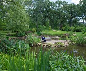 A woman in a blue dress relaxes on a bench by the pond at the R.W. Norton Art Gallery and Botanic Gardens in Shreveport.