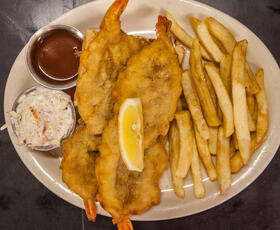 A Shrimp Buster sandwich with fries, coleslaw and dipping sauce, garnished with a lemon.