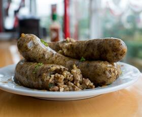 Several boudin sausages sit on a white plate. One of the sausages is cut, revealing the rice and meat inside.