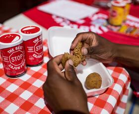 Hands break a boudin ball apart against a white- and red-checkered tablecloth.