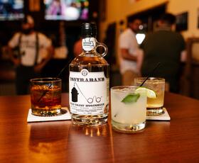 A bottle of moonshine sits next to a variety of cocktails on a wooden table at Bayou Terrebonne Distillers.