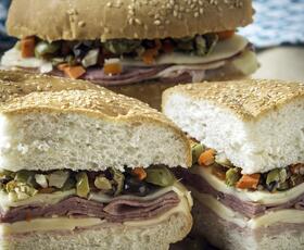 Sliced muffuletta sandwiches stacked with layers of meat, cheese and olive tapenade on sesame bread.