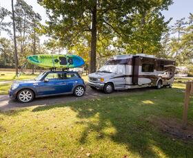 RV and car with kayaks parked under trees at Fairview-Riverside State Park’s grassy campground.