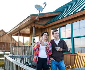 Couple enjoying morning coffee on a waterfront cabin deck at Fontainebleau State Park with fishing poles nearby.