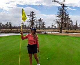 Golfer standing on the green at TPC Louisiana holding the flagstick near the hole.