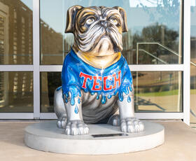 A painted bulldog statue wearing a blue “TECH” shirt stands proudly outside a building on the Louisiana Tech University campus.
