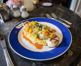 A plated dish of seared scallops with colorful garnish sits on an elegant table setting inside the Carriage House restaurant.