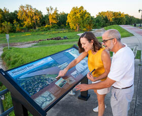 A couple smiles while reading an interpretive sign overlooking the scenic Mississippi River and surrounding greenery.