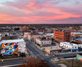 An aerial view of downtown Ruston captures colorful murals and historic buildings beneath a glowing pink and orange sunset sky.