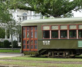 Historic green St. Charles streetcar travels past oak trees and homes along St. Charles Avenue.