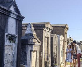 Visitors walk among above-ground tombs at St. Louis Cemetery No. 1 in New Orleans, with historic stone mausoleums lining a gravel pathway.
