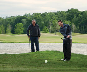 Two golfers in action on the course at Atchafalaya at Idlewild near a pond and wooded area.