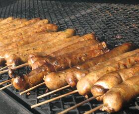 Boudin sausage on a stick, roasting over an open grill.