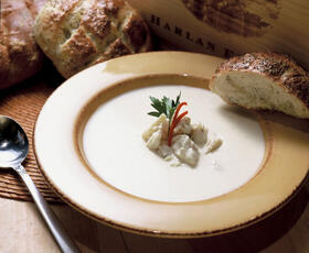 A yellow bowl filled to the brim with a milky white soup, topped with lumps of crab meat, herbs and a slice of crusty bread.