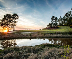 Cypress Bend Golf Resort at dusk, with a blue, slightly pink sky, with a pond and tall trees in the background.