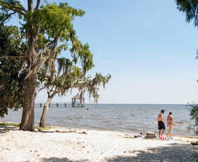 A couple wearing bathing suits walks in the water at Fontainebleau State Park beach.