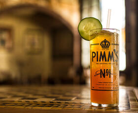 A vibrant orange cocktail, garnished with a cucumber slice, on a table at Napoleon House in New Orleans, Louisiana.