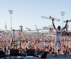 Trombone Shorty raises his instruments above his head while performing at Jazz Fest.