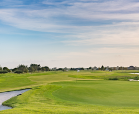 A wide shot of LaTour Golf Course with smooth green fairways and a calm, blue, slightly cloudy sky.