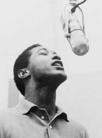 Sam Cooke croons into a microphone hanging above him; his eyes are closed and he wears a light-colored collared sweater