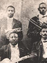 Four men stand with a bass, trumpet, trombone and clarinet, while two sit with guitars in a sepia-toned setting