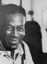 Son sites in a chair, holding his guitar, smiling to the camera