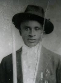 A black and white photo of Amede Ardoin dressed in a suit and jaunty hat