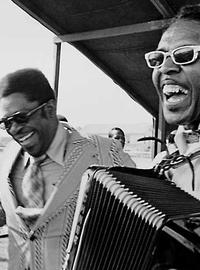 A black-and-white image of three men with zydeco instruments, including an accordion. They all lauugh at the camera.