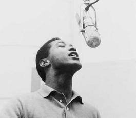 Sam Cooke croons into a microphone hanging above him; his eyes are closed and he wears a light-colored collared sweater