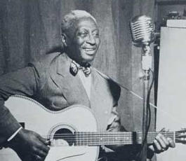 Leadbelly sits with his guitar in front of a microphone in a recording studio
