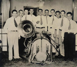 A group of men in white shirts and tie gather around a drum set