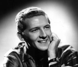 Under a spotlight, Jerry poses for a portrait. He wears a striped shirt and rests his chin on one arm.