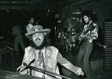 Dr. John sits at a piano singing enthusiastically while a man plays guitar behind him