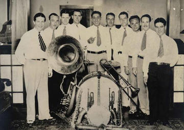 A group of men in white shirts and tie gather around a drum set