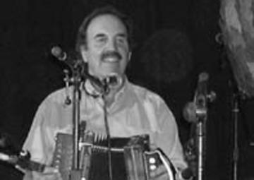 Mark sits with an accordion in his lap in front of two microphones preparing to play