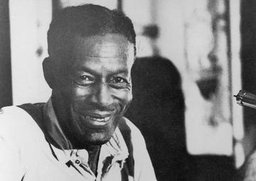 Son sites in a chair, holding his guitar, smiling to the camera