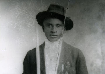 A black and white photo of Amede Ardoin dressed in a suit and jaunty hat